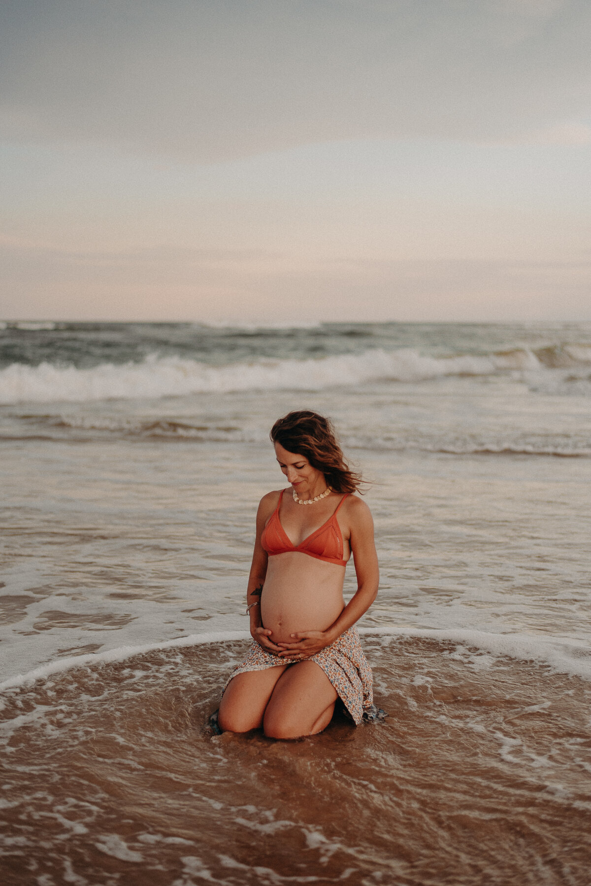 Chrissy Beth during pregnancy, kneeling in shallow waves at the beach.